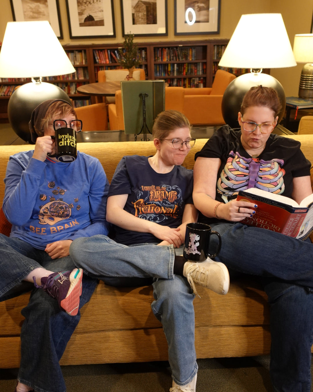 Three people sitting together in a casual setting, reading books and drinking from mugs.