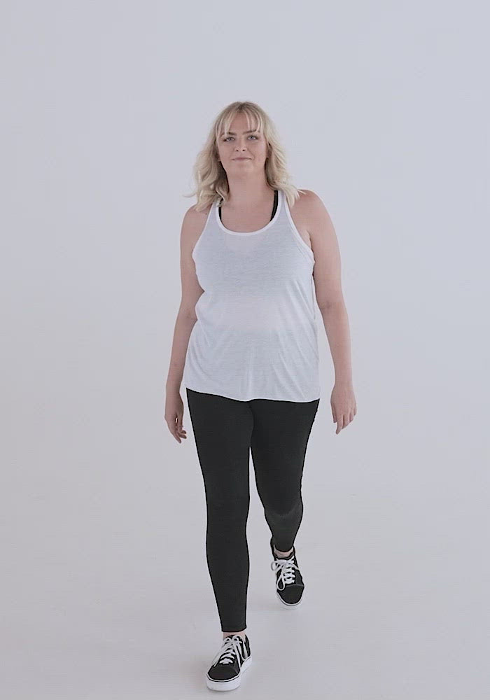 video of white woman with medium build and blonde hair showing the Flowy racerback tank fit. Loose fit with soft material, white tank can be sheer and show colors of clothes underneath. Black is not as sheer. Neckline is high covering most of the chest.