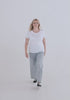 Video of white woman with blond hair showing the fit of the Relaxed Fem Fit Tee. It hugs curves, has a high crew neck neckline, sleeves can be a bit small on this, hemline flows below pants line.