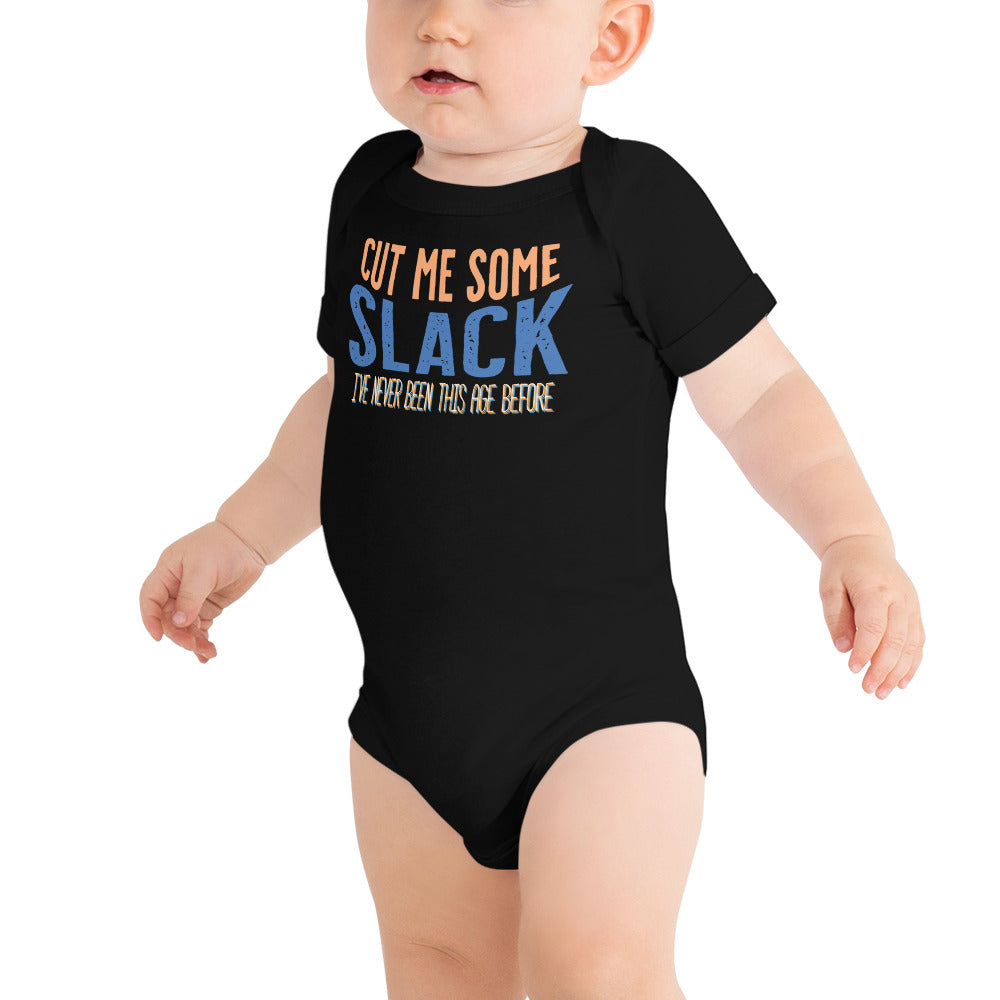 Model of white baby wearing black baby onsie with “Cut me some” in orange “Slack” in blue. “I’ve never been this age before” in smaller text underneath. 