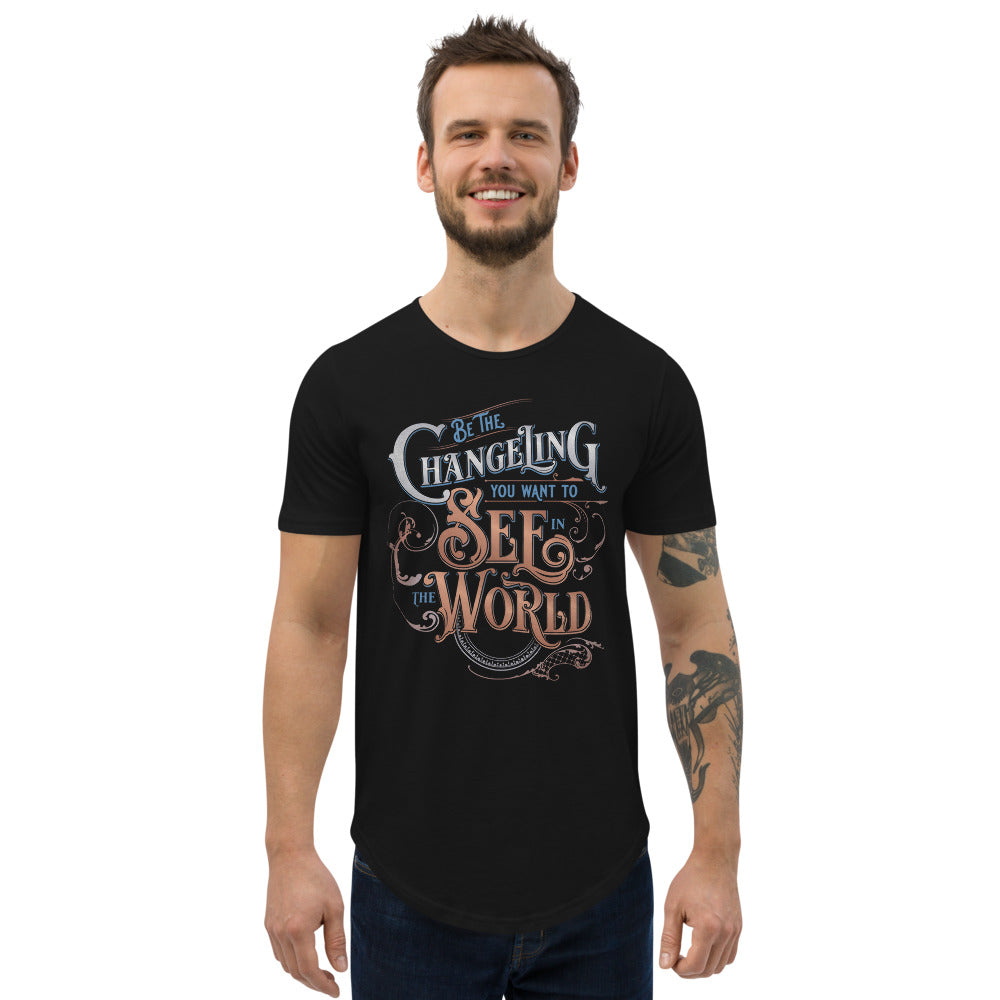 MOdel of white man with slender build with dark hair and beard wearing Black masc fit curved hem Tee with “Be the Changeling you want to see in the world” in silver, bronze and blue lettering surrounded by intricate decals