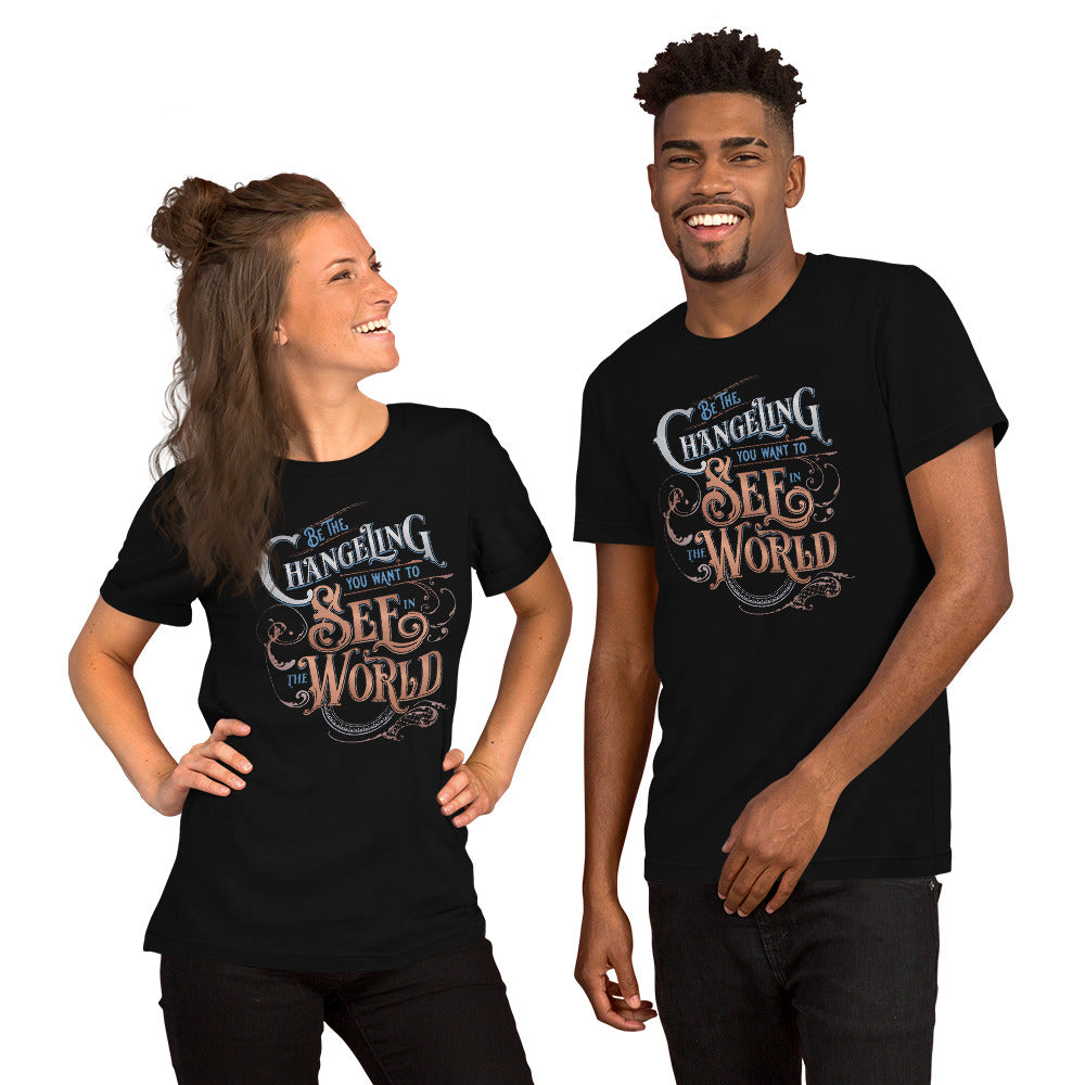 Two models standing side by side in playful poses. One white woman, hands on hips, with half her brunette hair in a bun, and the other half draping past her shoulders. On the right is a tall black man with a goatee. They are both wearing the Unisex Tee with  “Be the Changeling you want to see in the world” in silver, bronze and blue lettering surrounded by intricate decals
